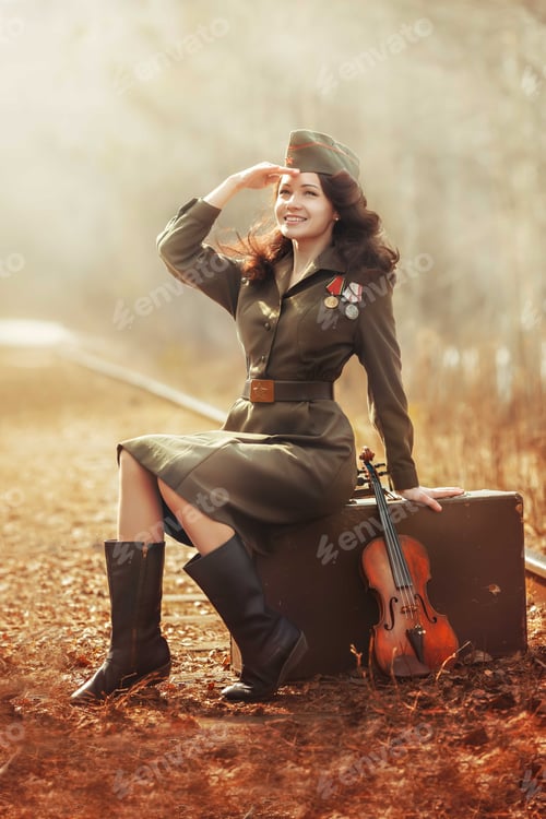 Preview: young woman with ringlets on military uniform sitting on vintage suitcase railway tracks with violin