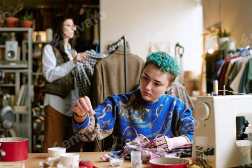 Preview: Young Adult Caucasian Woman Sewing Fabric While Middle Aged Woman Browsing Clothes