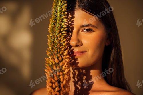 Preview: Young woman with long dark hair holds a vibrant plant close to her face