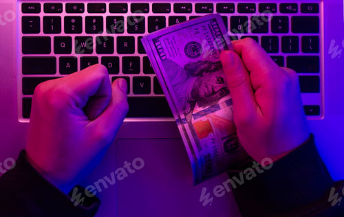 Preview: Money in male hands on the background of a laptop keyboard in neon lighting.