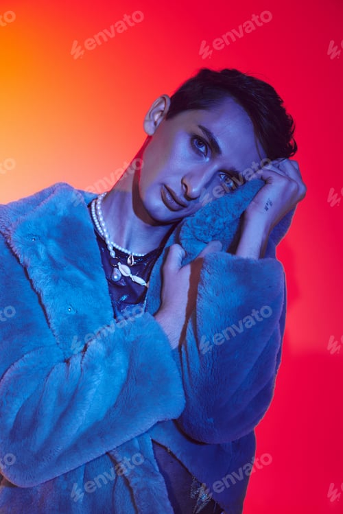Preview: sophisticated androgynous man in purple faux fur posing on vibrant backdrop and looking at camera