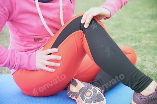 Preview: Female athlete suffering form running knee or kneecap injury during outdoor workout on dirt road.