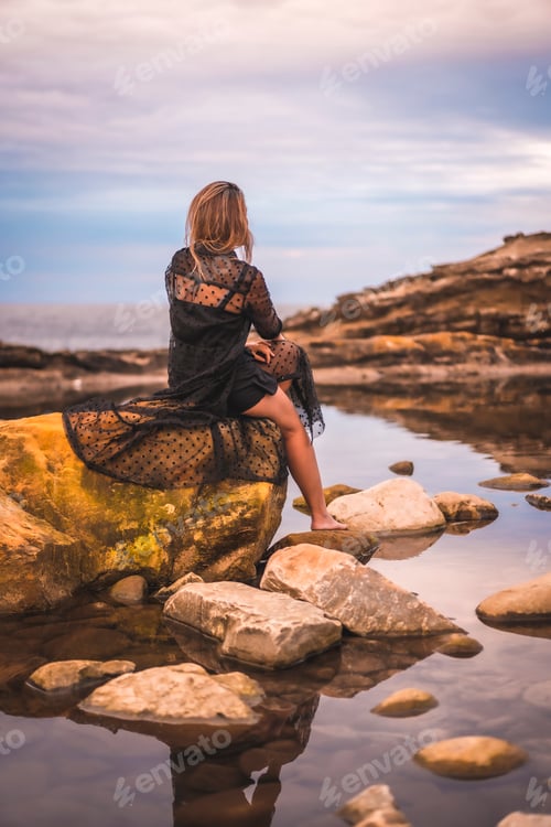 Preview: Young brunette Caucasian woman in a long black transparent dress on some rocks