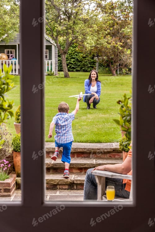 Preview: Mother watching son play in garden with toy airplane