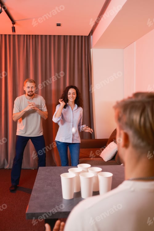 Preview: Group of friends playing a game of beer pong in a cozy setting