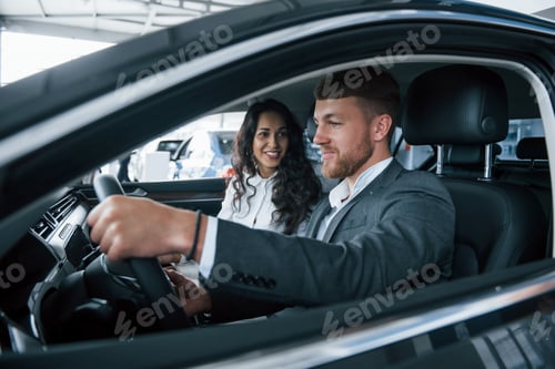 Visualização: Pessoas felizes. Adorável casal de sucesso experimentando um carro novo no salão de automóveis