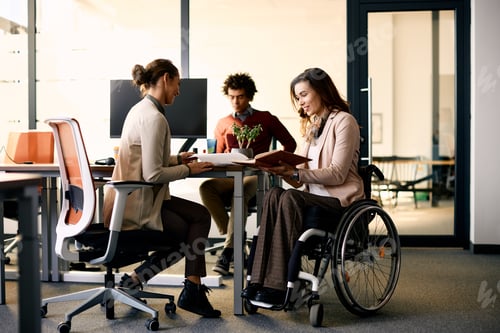 Preview: Happy businesswoman in wheelchair going through reports with her colleague in the office.