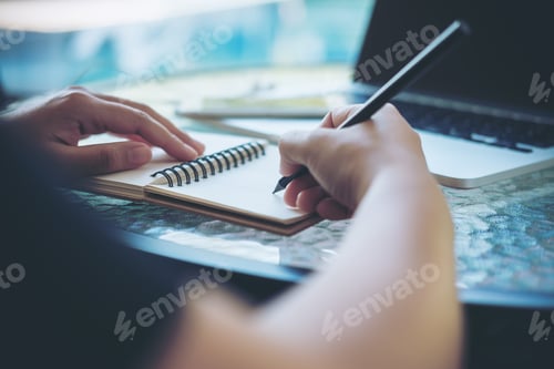 Preview: A woman working and holding black pencil and writing on notebook on glass table