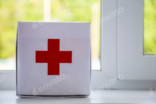 Preview: White first aid kit with red cross indoors on windowsill on blurred background. Healthcare concept
