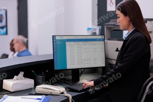 Preview: Reception worker checking patient examination report on computer working in hospital waiting room