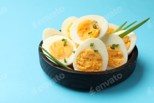 Preview: Halves of hard boiled eggs with green onions on light blue background, closeup