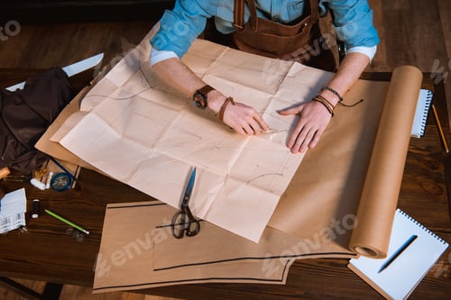 Preview: cropped shot of male fashion designer in apron making sewing patterns at workplace