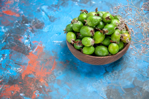 Preview: Front view of delicious vitamin bomb fresh feijoas in a brown pot on wooden tray on blue table