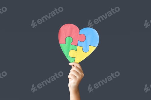 Preview: Hand Holding a Heart Made of Color Puzzle on Gray Background. Autistic Disorder Concept.