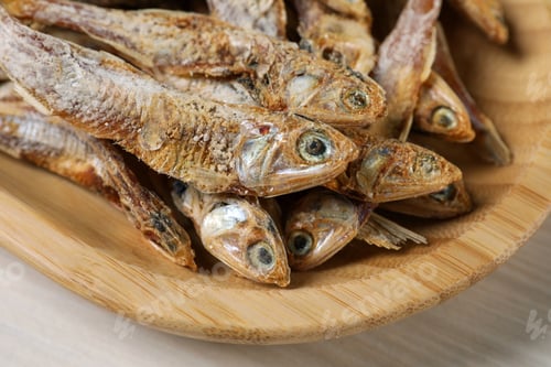 Preview: Wooden plate of tasty dried anchovies on table, closeup