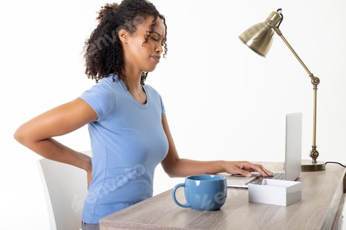 Preview: African american mid adult woman with backache using laptop by cup and lamp on table, copy space