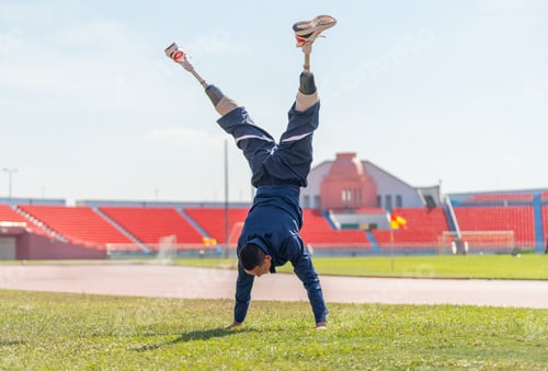 Preview: Sport man athlete with a prosthesis on his leg warm up the body with do the handstand in grass field