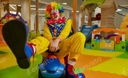 Preview: Overjoyed clown having fun riding toy car at playroom