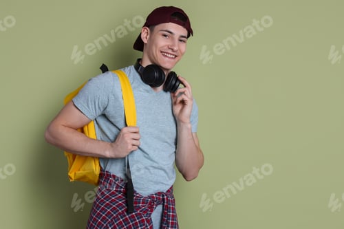 Preview: Student with headphones and backpack on olive background, space for text
