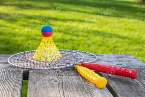 Preview: Badminton game rackets and shuttlecock on wooden table with green grass in the park on a sunny day