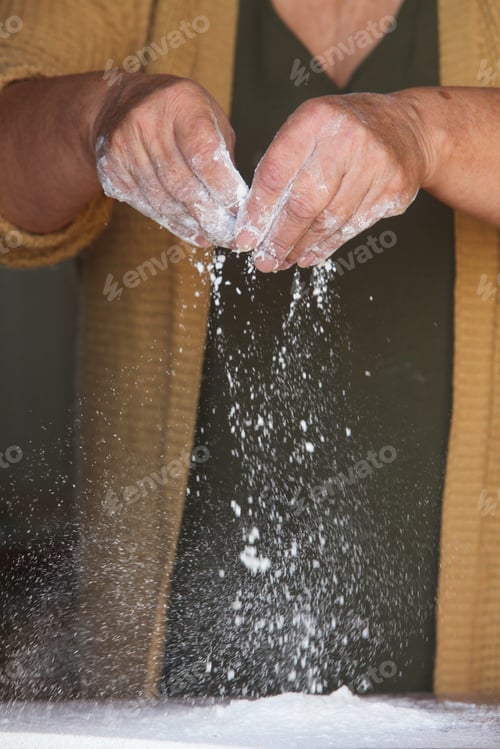 Preview: Closeup of Senior Woman’s Hands Sprinkling Flour on Wooden Table