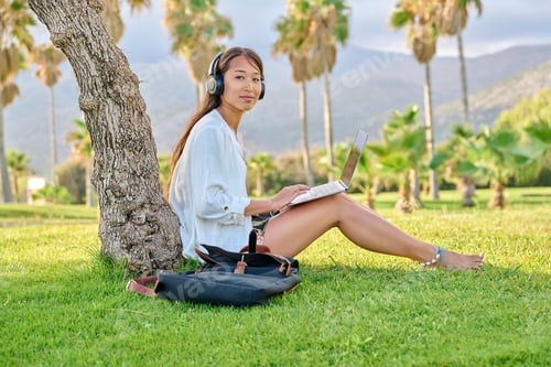 Preview: Young woman in headphones working on a laptop outdoors