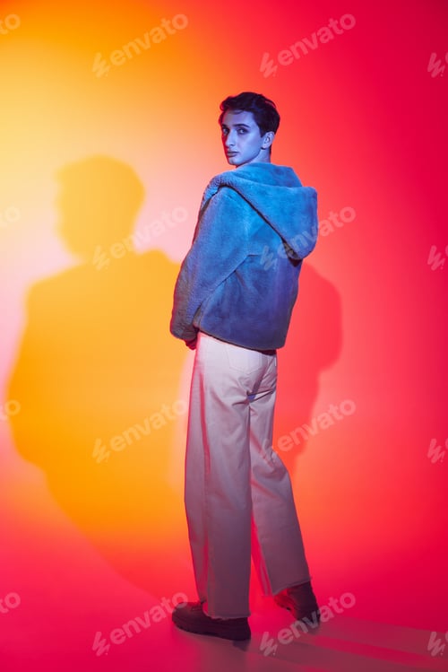 Preview: well-dressed androgynous man in purple faux fur posing on vibrant backdrop and looking at camera