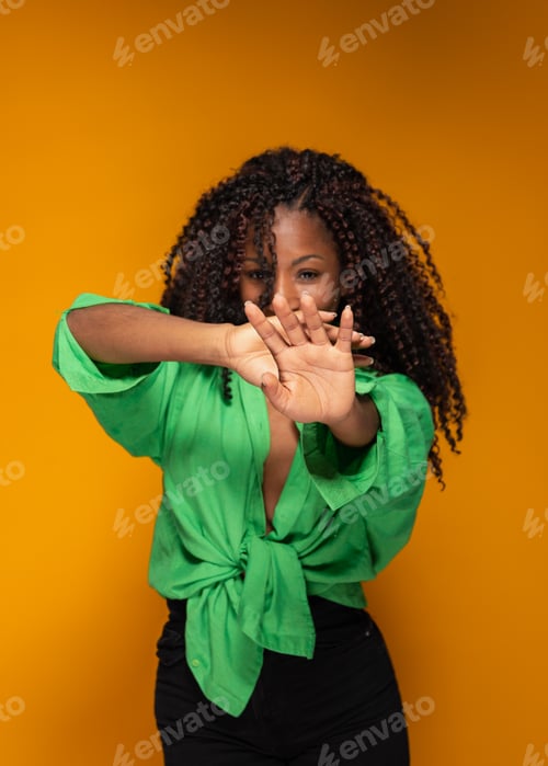 Preview: Studio shot of Hispanic woman in green shirt making stop sign with hand on yellow background