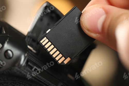 Preview: Man inserting SD memory card into photo camera indoors, closeup