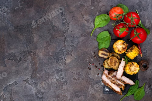 Preview: sliced pork steak and grilled vegetables on slate board on stone table.