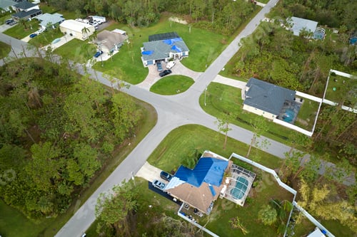 Preview: Aerial view of damaged in hurricane Ian house roof covered with blue protective tarp