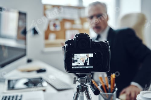 Preview: Senior man in elegant business suit using modern technologies while making social media video