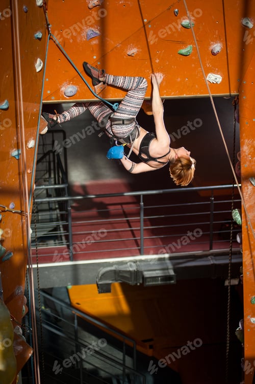 Preview: Female climber is climbing up on indoor rock-climbing wall