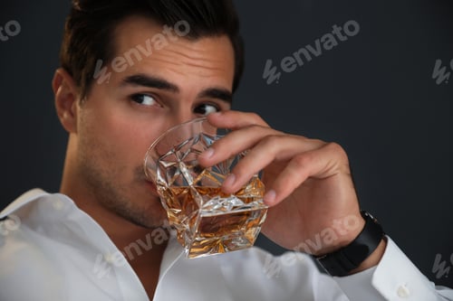Preview: Young man with glass of whiskey on dark background