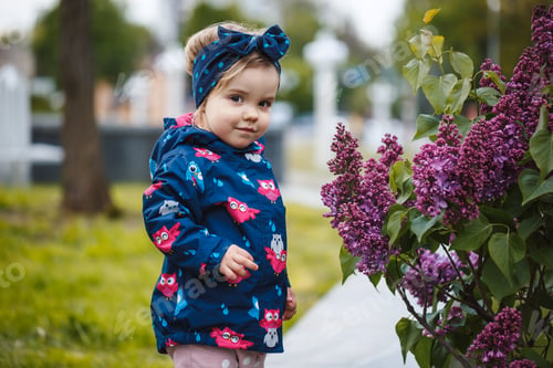 Preview: A little girl stands near a lush bush of lilacs, she smiles and sniffs purple flowers