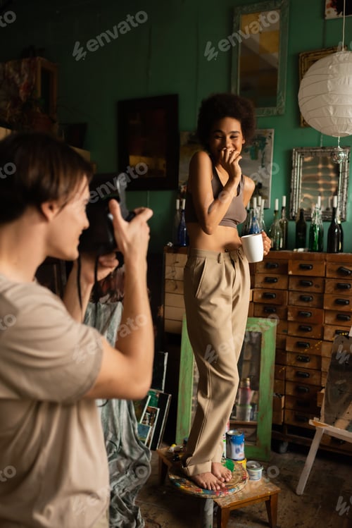 Preview: blurred man with vintage camera taking photo of african american girlfriend standing on stool