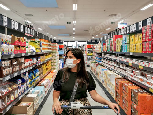 Preview: Young woman wearing face mask in groceries store to by essentials for quarantine during covid.