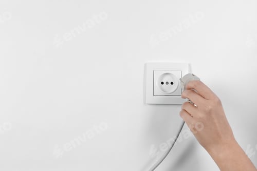 Preview: Woman putting plug into power socket on white background, closeup. Electrician's equipment