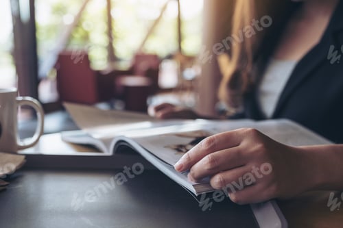 Preview: Closeup image of a business woman reading a book with coffee cup on table in cafe