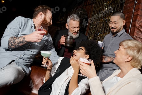 Preview: african american woman laughing near multiethnic friends with drinks in bar, after work party