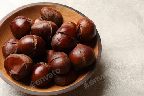 Preview: Fresh edible sweet chestnuts in wooden bowl on grey table, closeup
