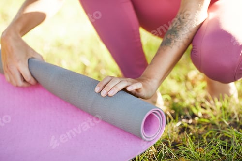 Preview: Woman Rolling Yoga Mat in Green Grass Outdoors
