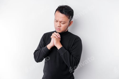 Preview: Religious Asian man wearing a black shirt praying to God, isolated by a white background.