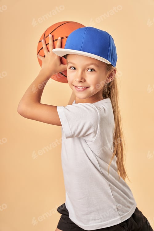 Preview: Adorable joyful girl in cap plying basketball