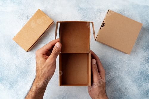 Preview: Parcel cardboard box in a man hands on a gray table background