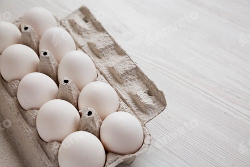 Preview: Uncooked Organic White Eggs in a paper box on a white wooden surface, side view. Copy space.