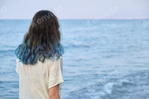 Preview: Fashionable young woman with dyed long blue hair walking along seashore