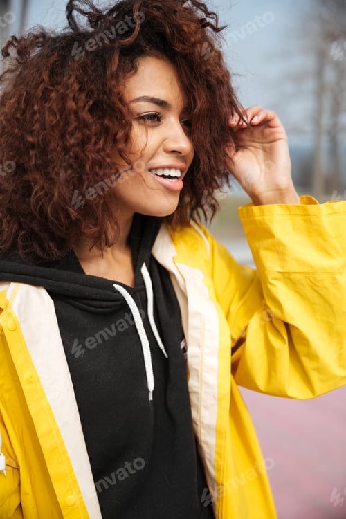 Preview: Happy african curly young woman wearing yellow coat