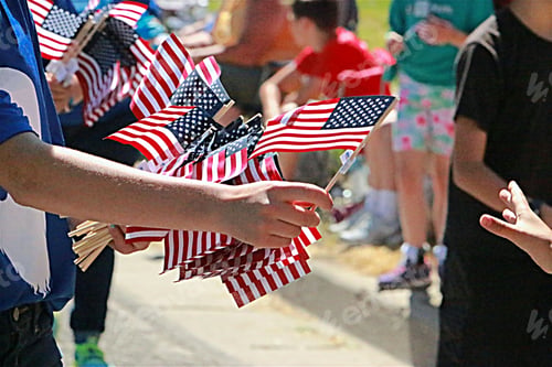 Preview: People passing out American flags along the street at a local Independence Day parade.