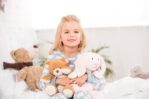 Preview: smiling adorable child sitting with soft toys on bed